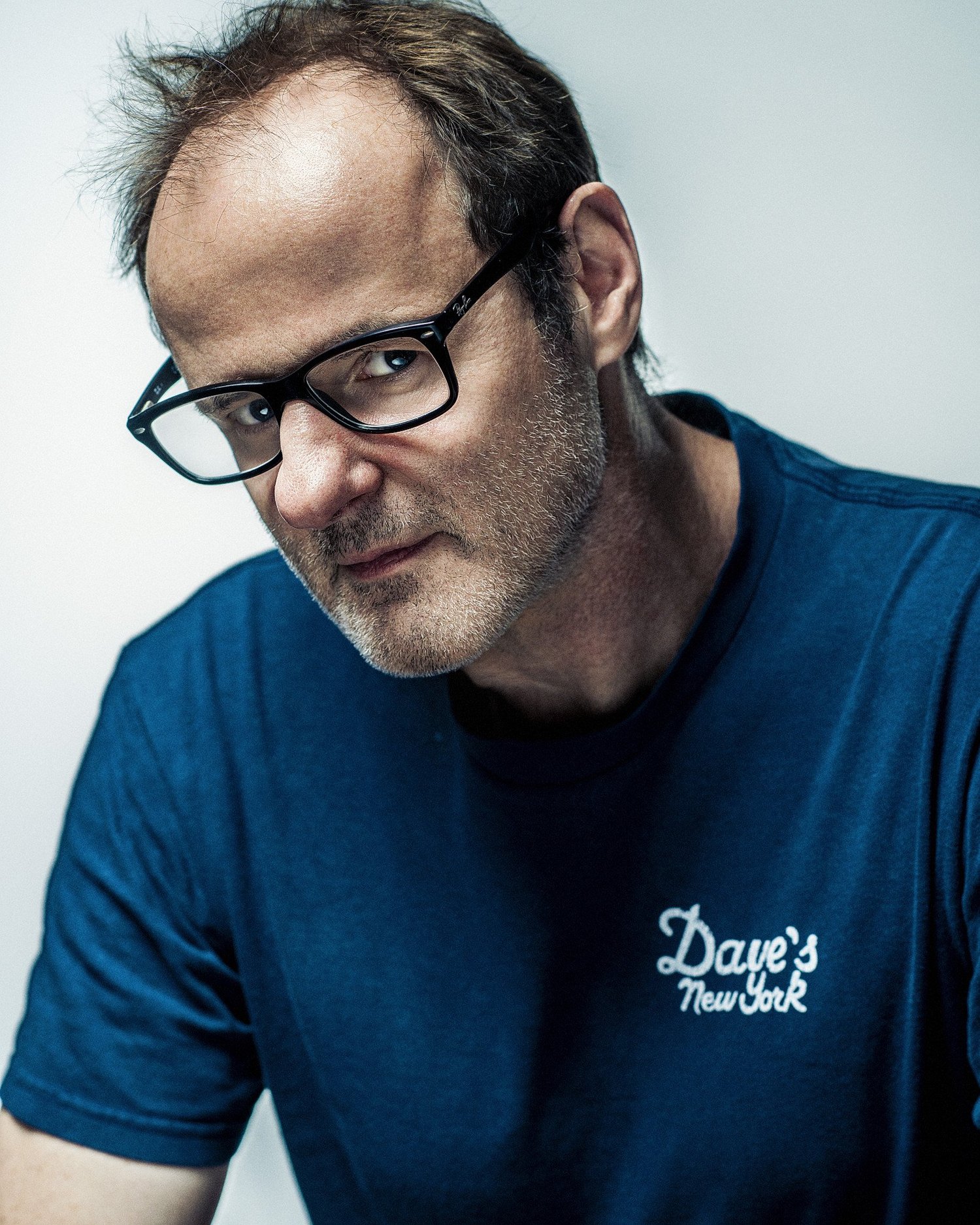 Vince Ebert ist ein deutscher Comedian, Kabarettist und Autor. Er trägt eine schwarze Brille und ein dunkelblaues T-Shirt mit dem weißen Schriftzug „Dave’s New York“.