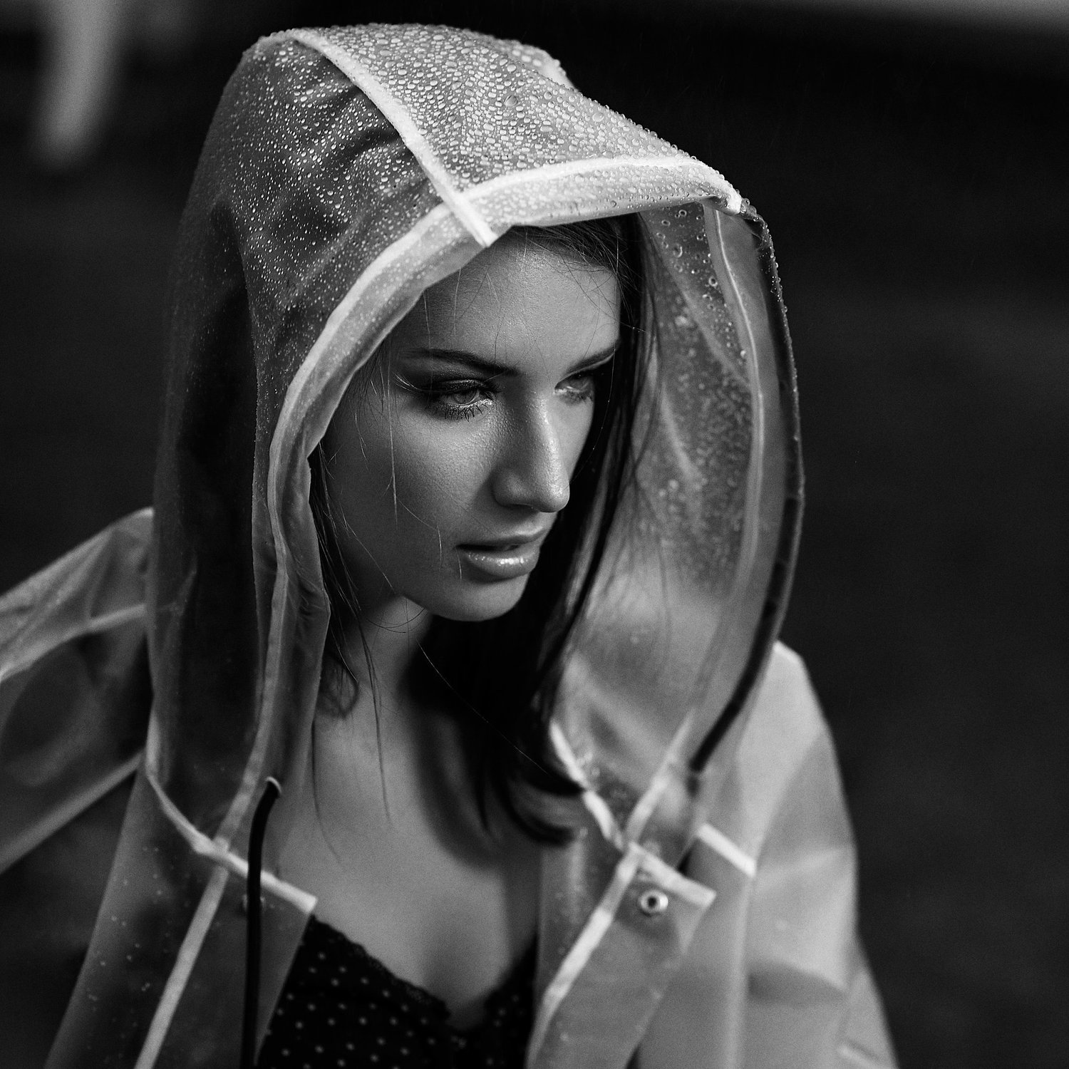 Schwarzweißfoto einer Frau in einem durchsichtigen Regenmantel mit Kapuze, die nass ist.