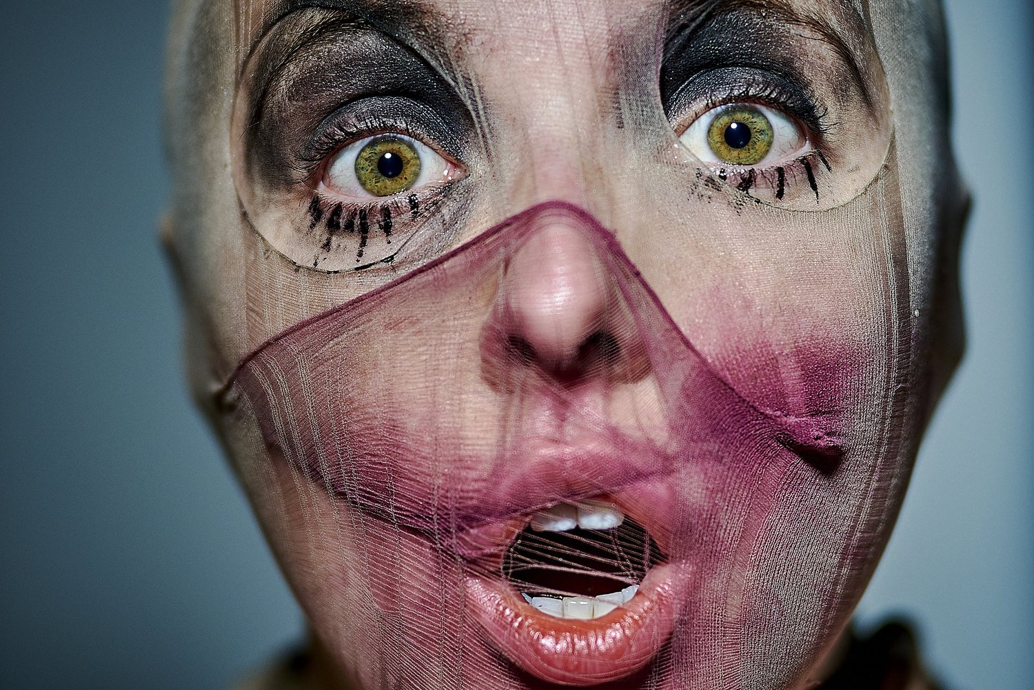 Nahaufnahme eines Gesichts mit einer Nylonstrumpfmaske, stark geschminkten Augen und offenem Mund.