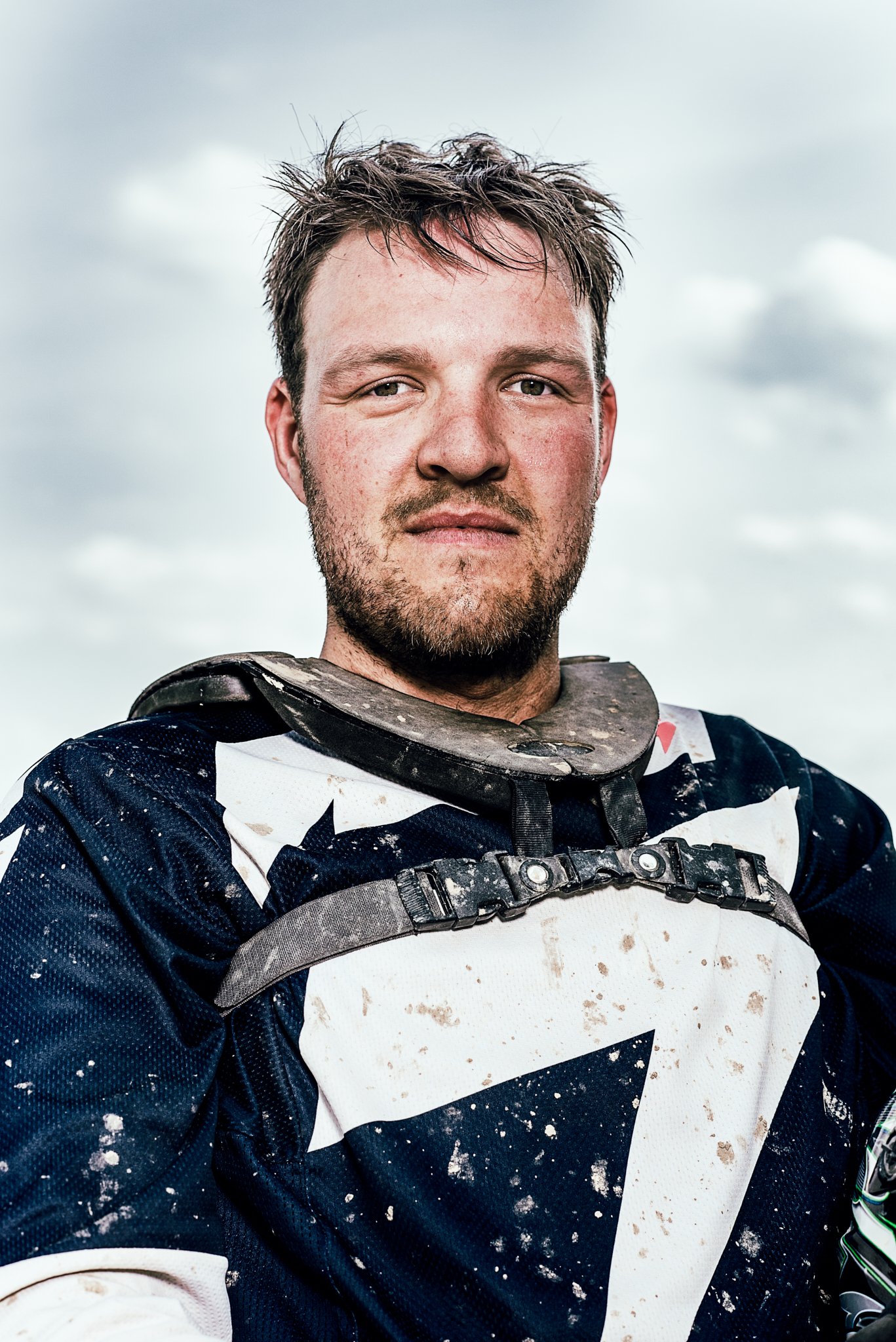 Porträt eines Mannes in Motorradschutzkleidung, leicht schmutzig, vor bewölktem Himmel.