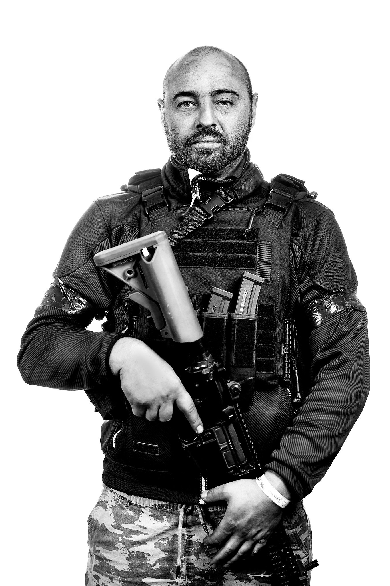Porträt eines Mannes in taktischer Weste mit Gewehr, Schwarz-Weiß Foto.