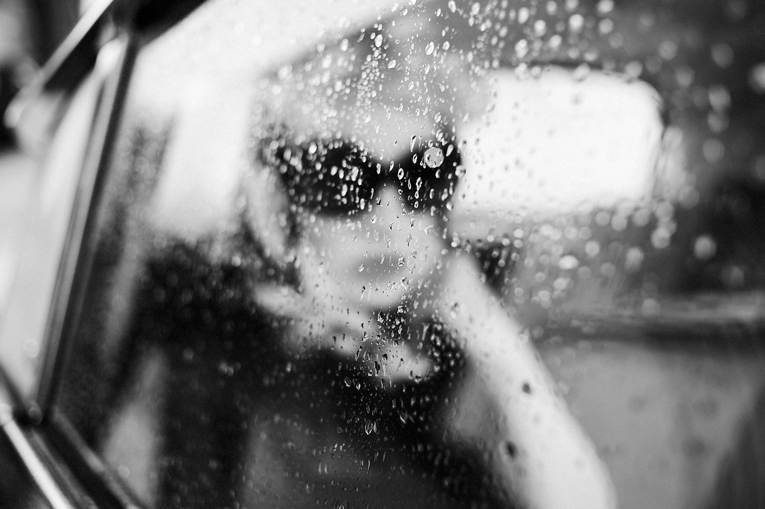 Verschwommene Person hinter regennassem Autofenster, Schwarzweißfoto
