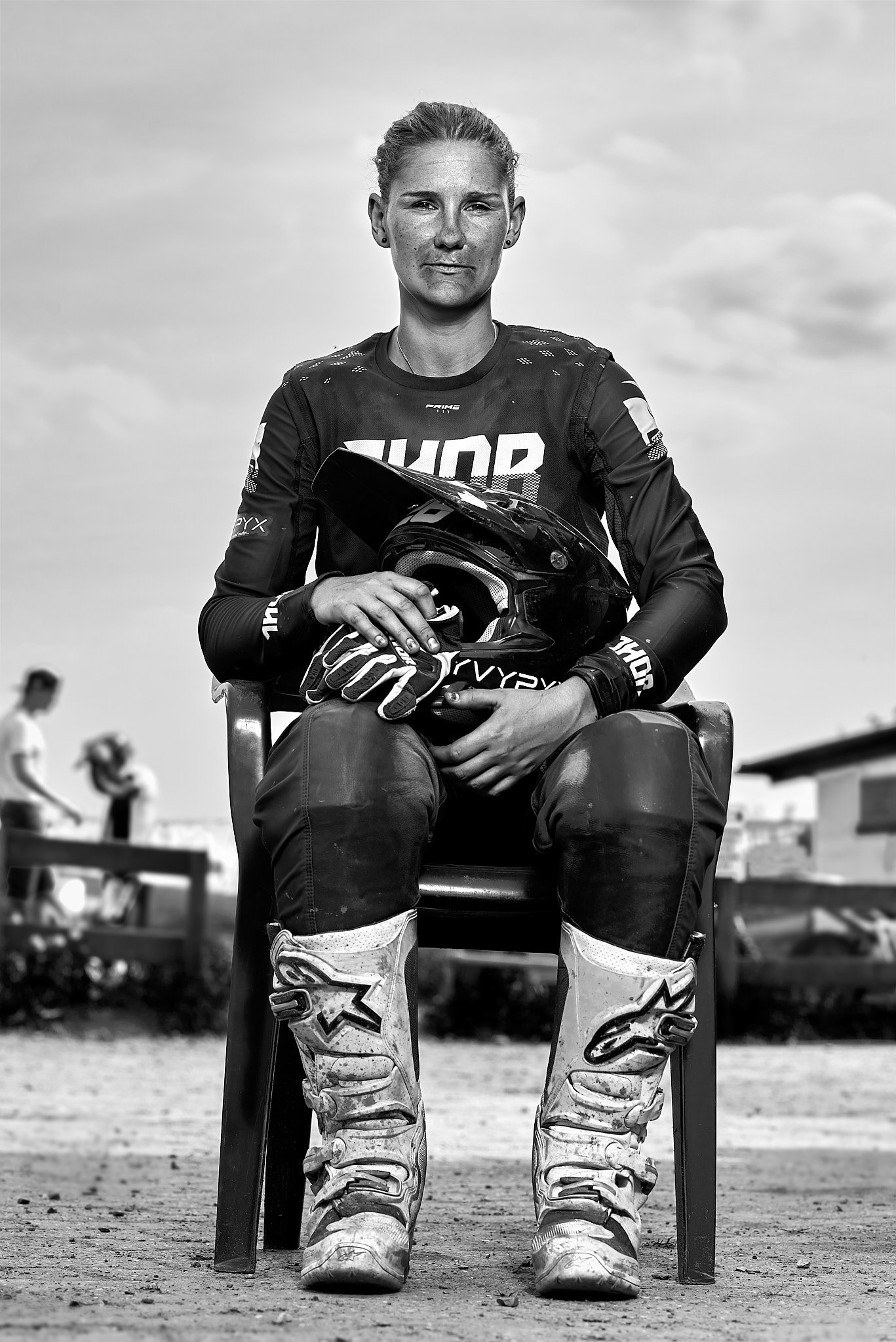 Motocross-Fahrer sitzt auf einem Stuhl, hält einen Helm und trägt Schutzkleidung.