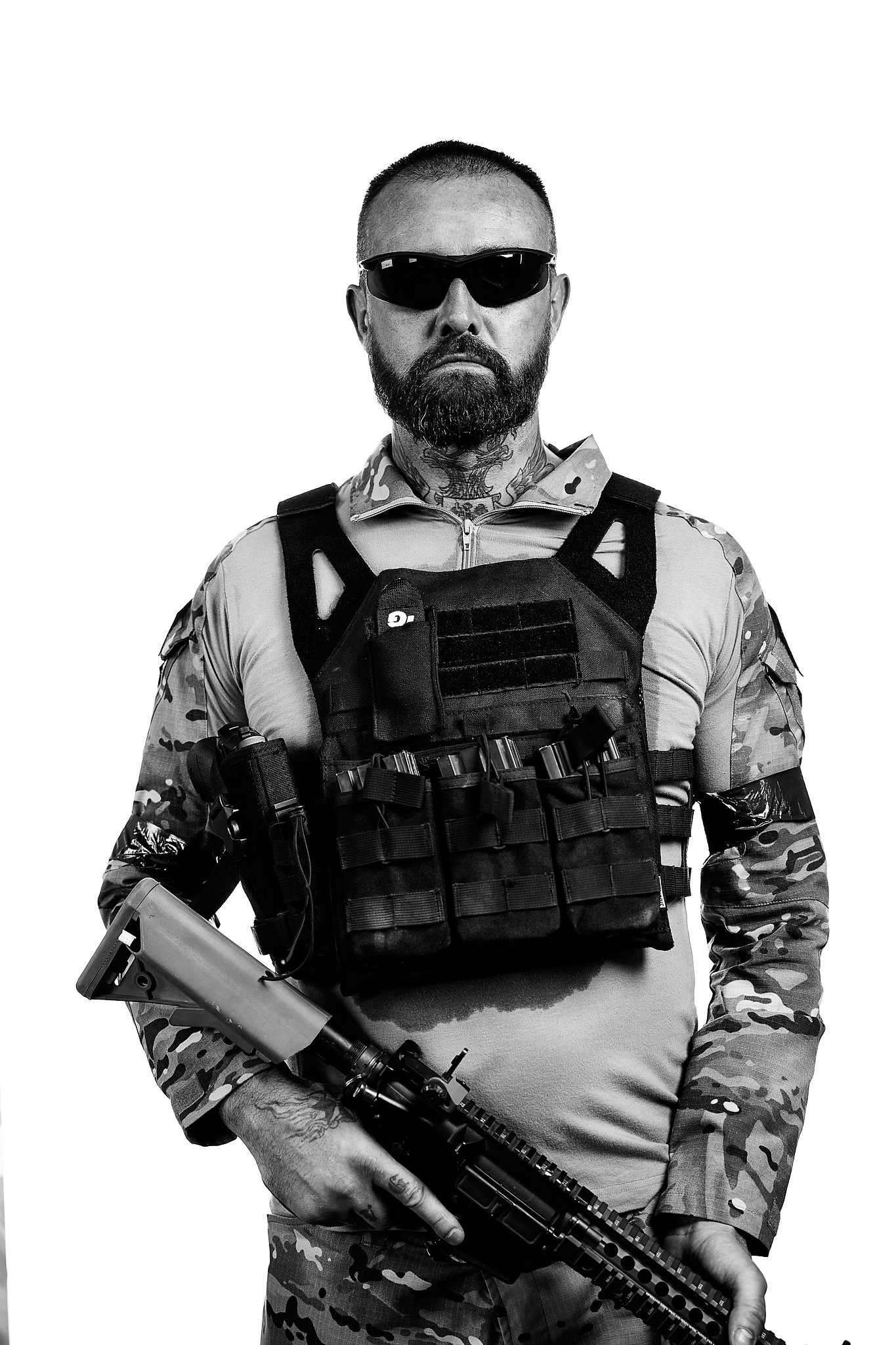 Mann in militärischer Ausrüstung mit Sonnenbrille hält ein Gewehr.