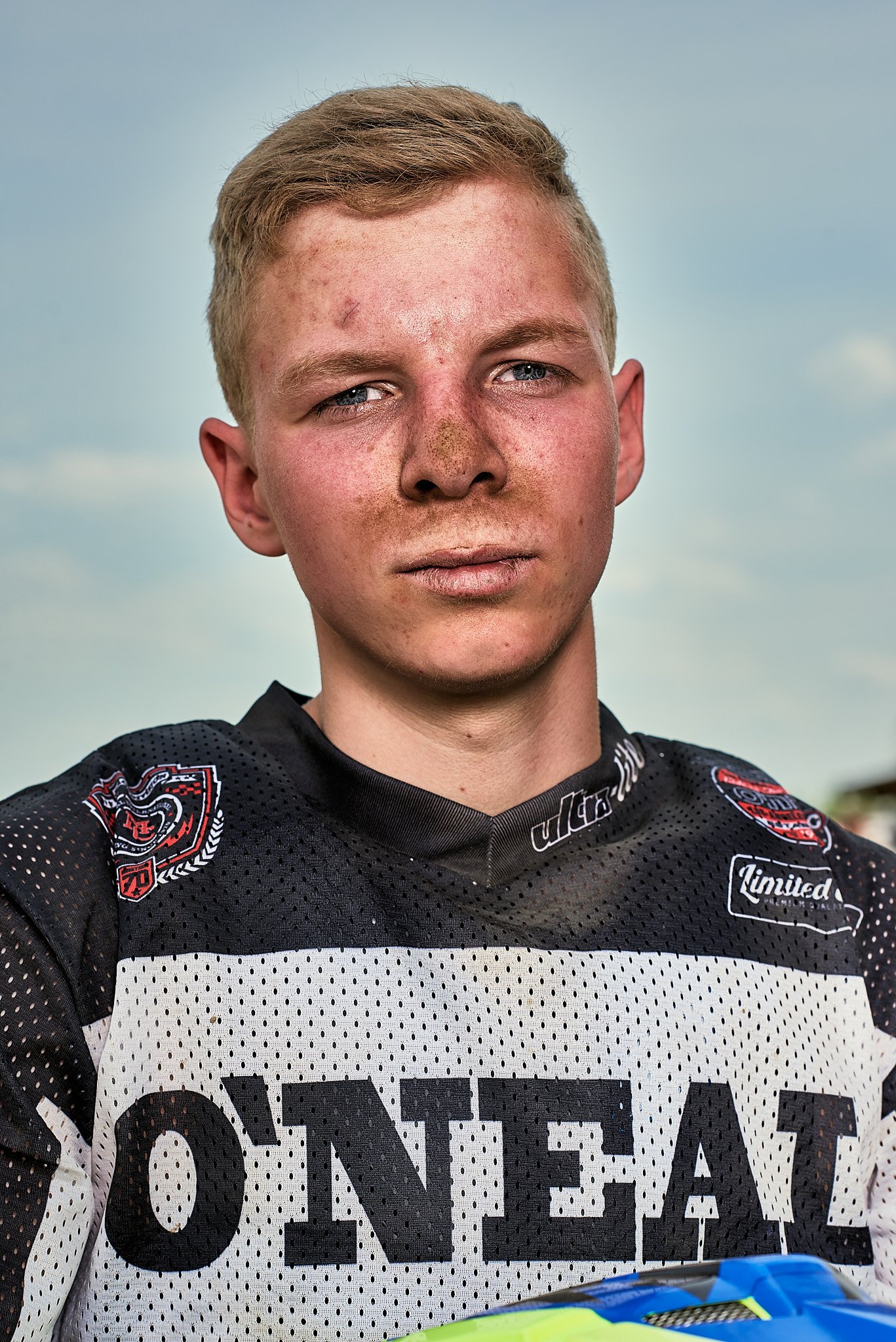 Junger Mann mit blondem Haar, verschmutztem Gesicht und einem schwarzen und weißen Offroad-Renntrikot mit der Aufschrift "O'NEAL".