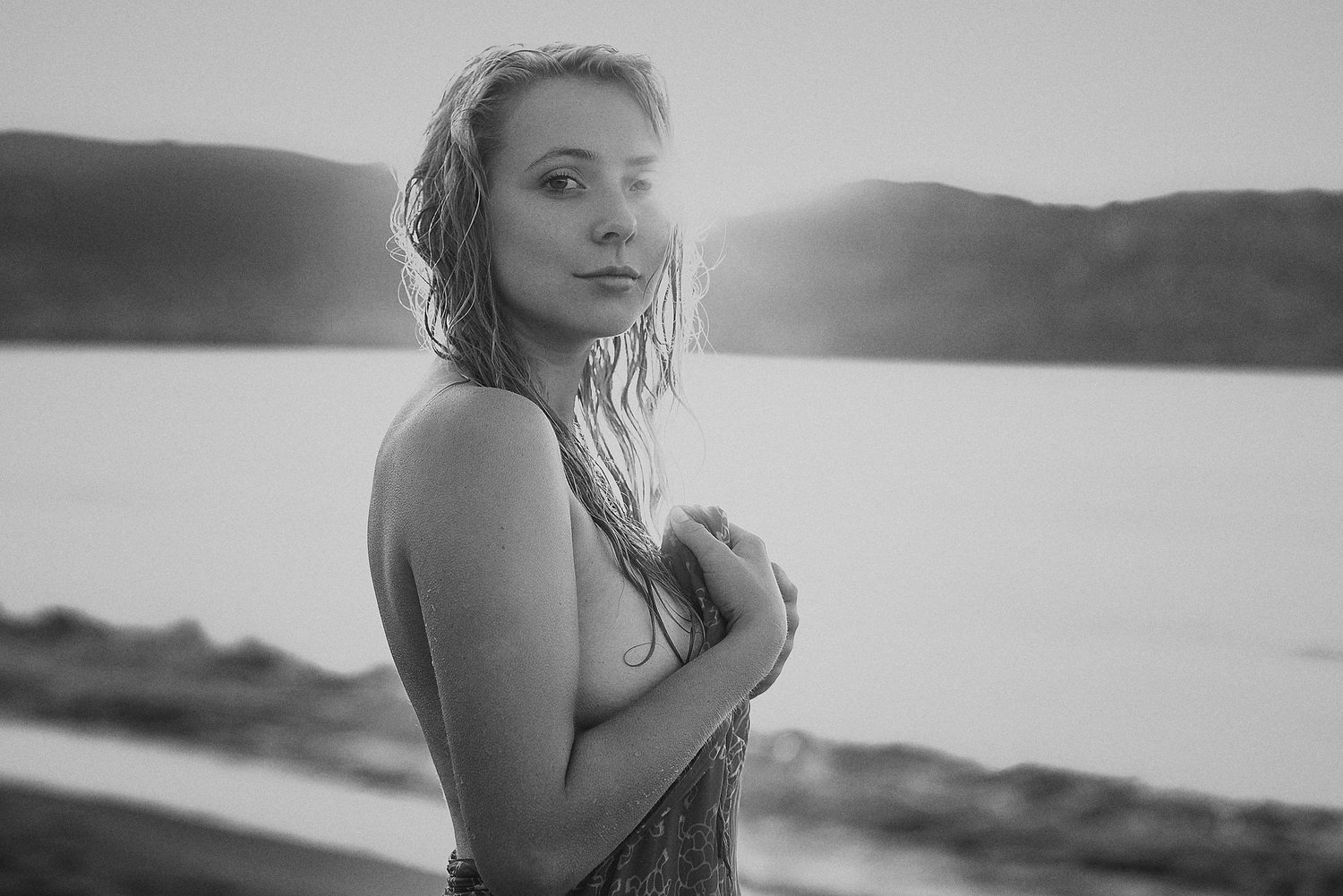 Schwarz-Weiß-Fotografie einer Frau mit nassen Haaren am Strand bei Sonnenuntergang.