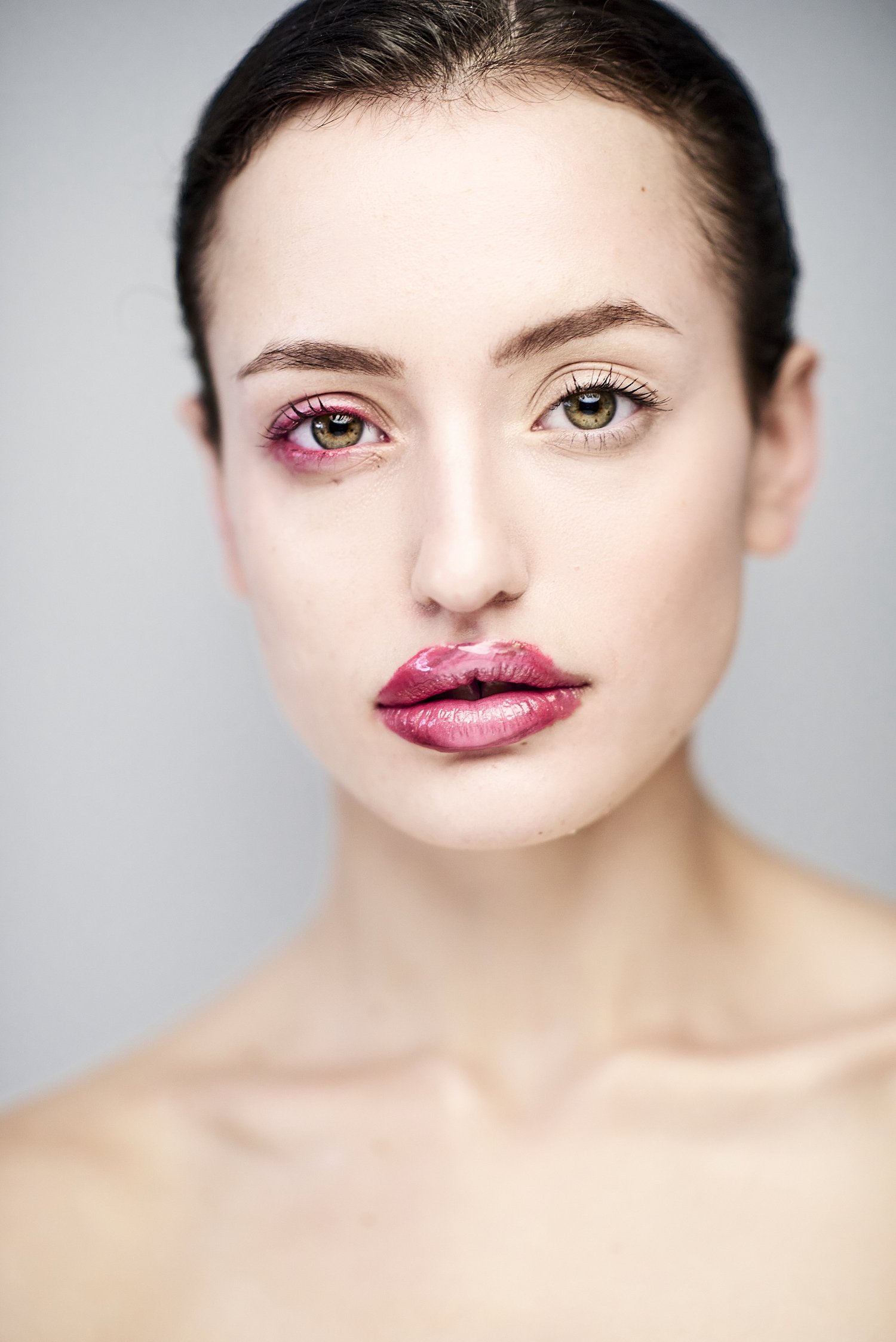 Nahaufnahme eines Gesichts mit ungleichmäßigem Make-up auf Augen und Lippen, halb professionell geschminkt, halb ungeschminkt, vor einem neutralen Hintergrund.