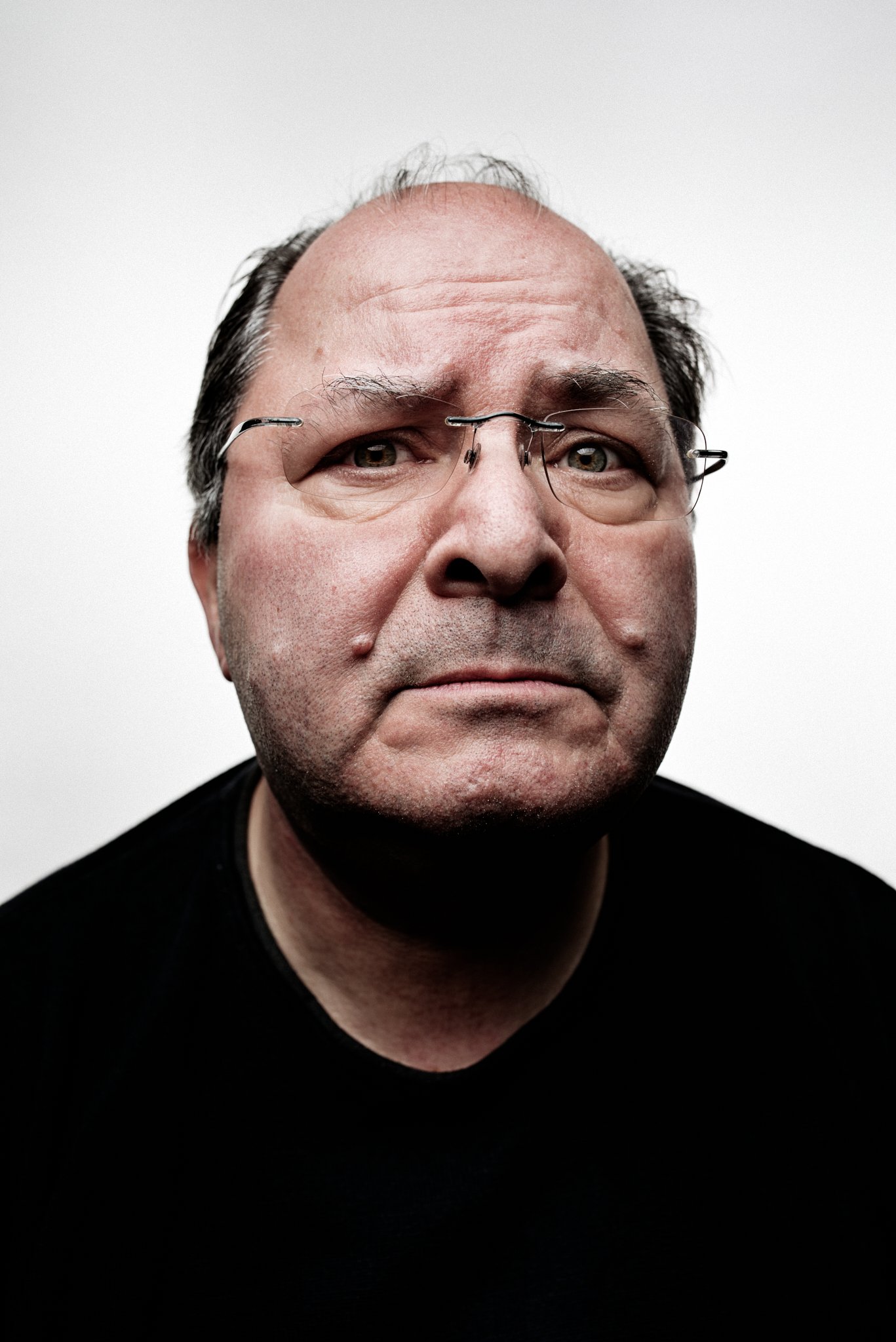 Porträt eines älteren Mannes mit Brille und nachdenklichem Blick.