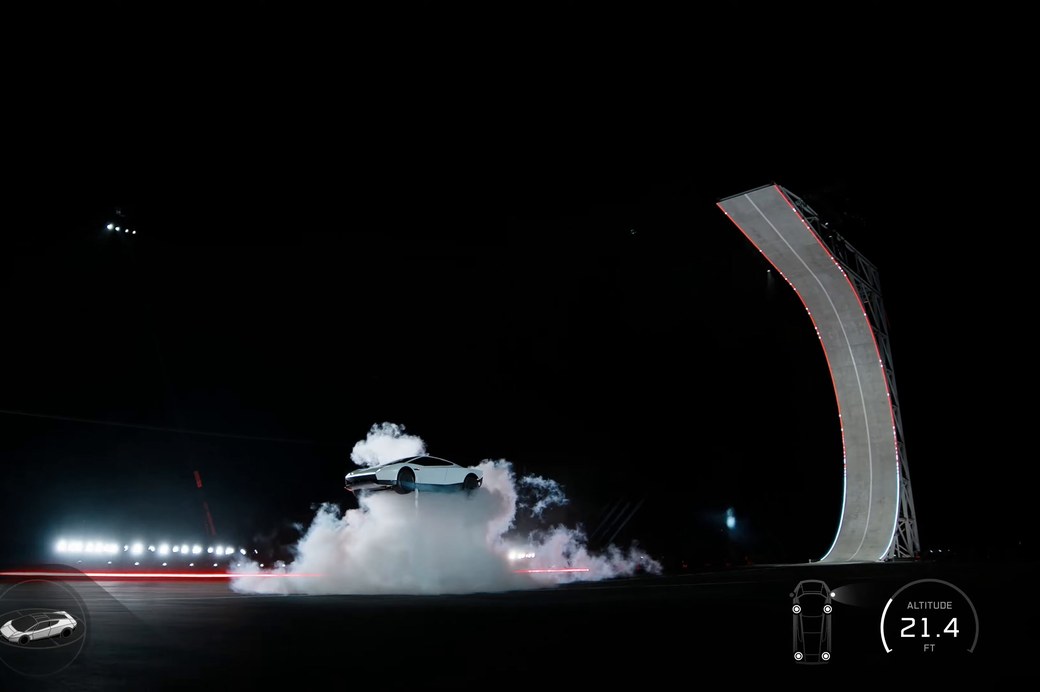 Nachtaufnahme: Ein weißer Sportwagen schwebt in einer dichten Rauchwolke knapp über einer Piste, rechts steht eine gebogene, rot beleuchtete Rampe, unten rechts die Einblendung ‚Altitude 21.4 ft‘.
